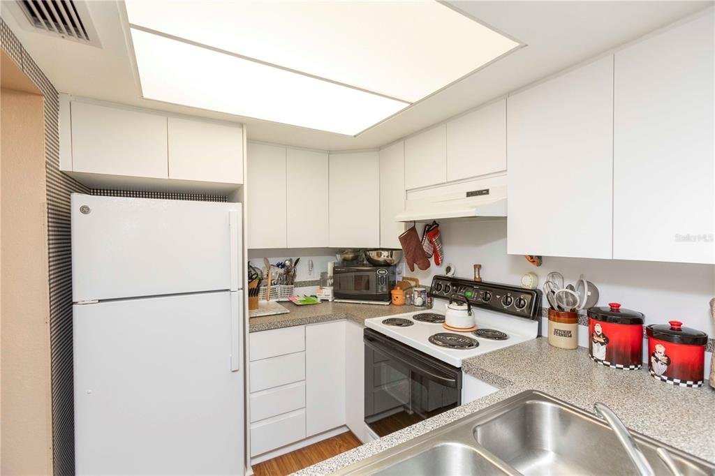 A kitchen features white cabinetry, a white refrigerator, a stove, and a stainless steel sink — 4726 MARINE PARKWAY UNIT 201, NEW PORT RICHEY, FL