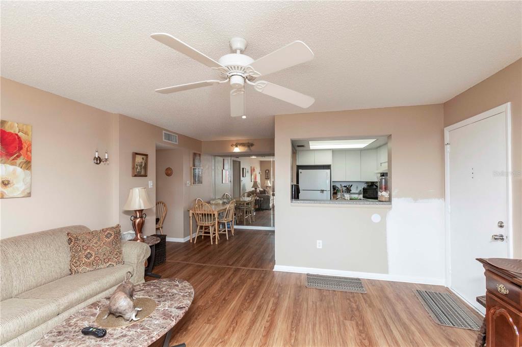 A living room with wood-look flooring, a ceiling fan, and an open view into the kitchen — 4726 MARINE PARKWAY UNIT 201, NEW PORT RICHEY, FL