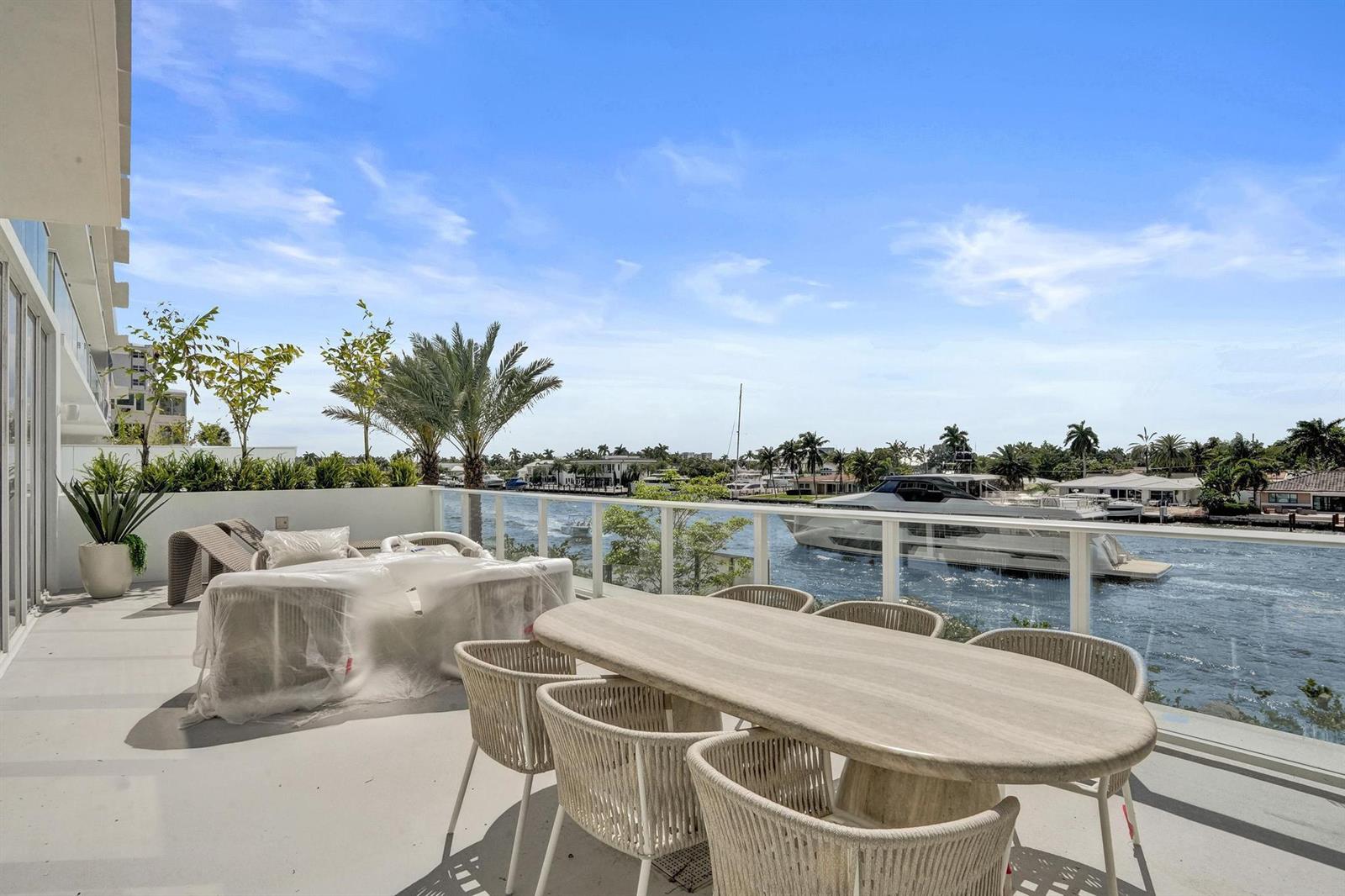 A balcony with outdoor furniture overlooks a waterway with a large yacht passing by — 407 N Riverside Drive # 203, Pompano Beach FL 33062, POMPANO BEACH, FL