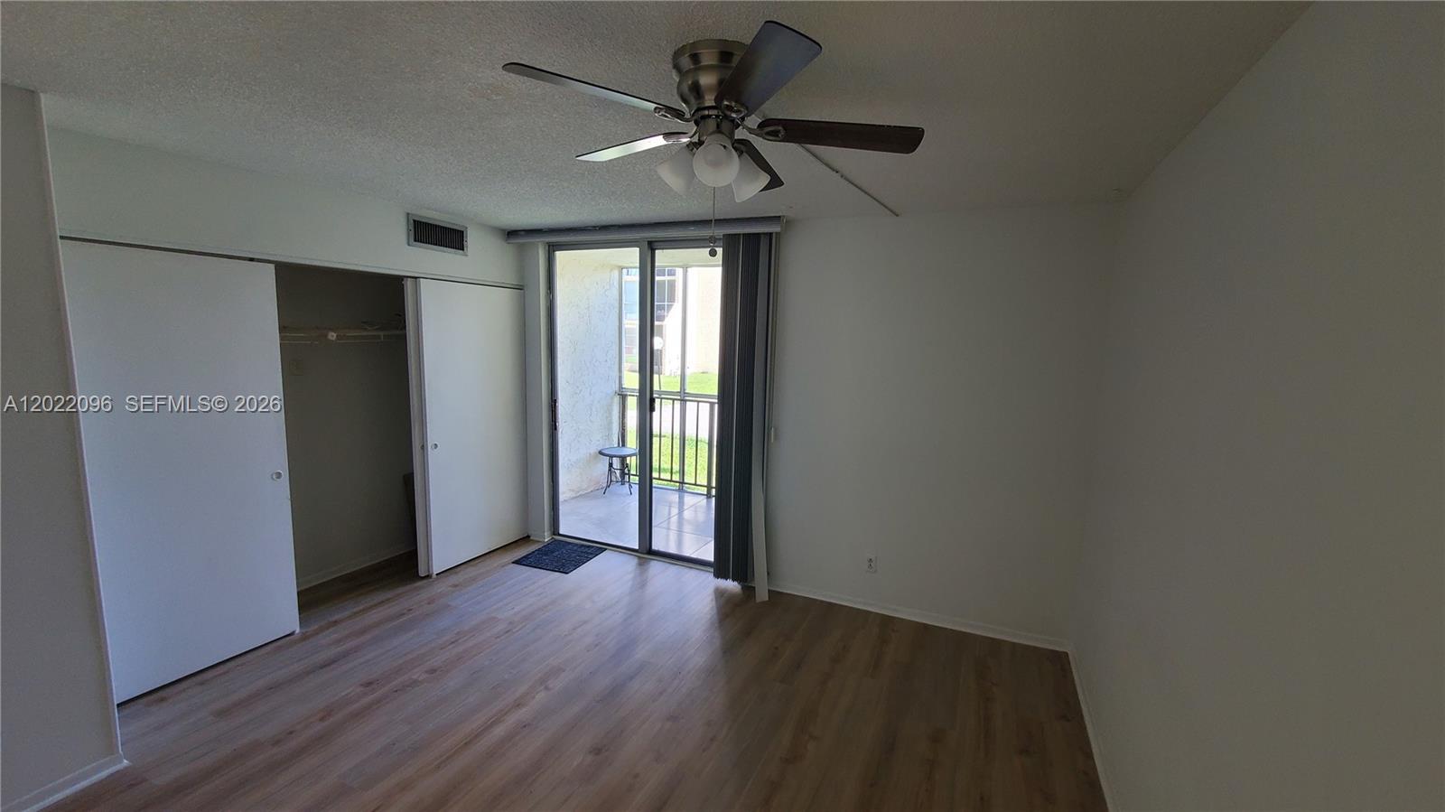 An empty bedroom features wood-look flooring, a ceiling fan, a sliding closet, and a balcony — 801 Three Islands Blvd # 109, Hallandale Beach FL 33009, HALLANDALE BEACH, FL