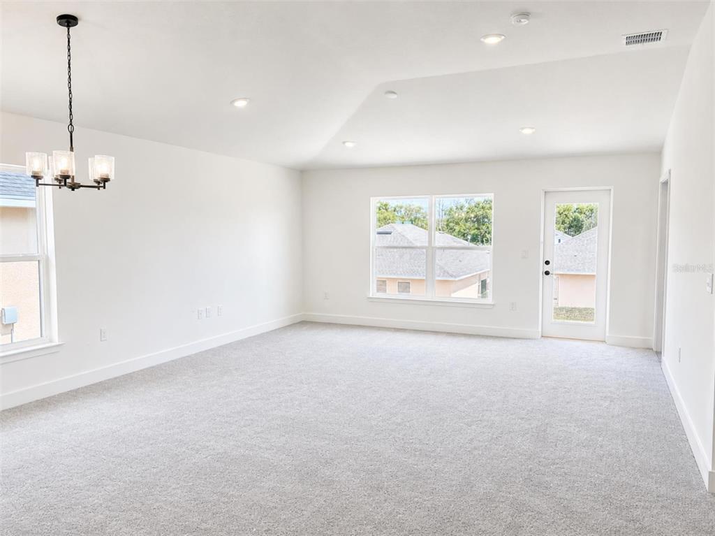 A bright, carpeted room features a vaulted ceiling, recessed lighting, a chandelier, and a door — 250 VERNY GROVE LANE, LEESBURG, FL