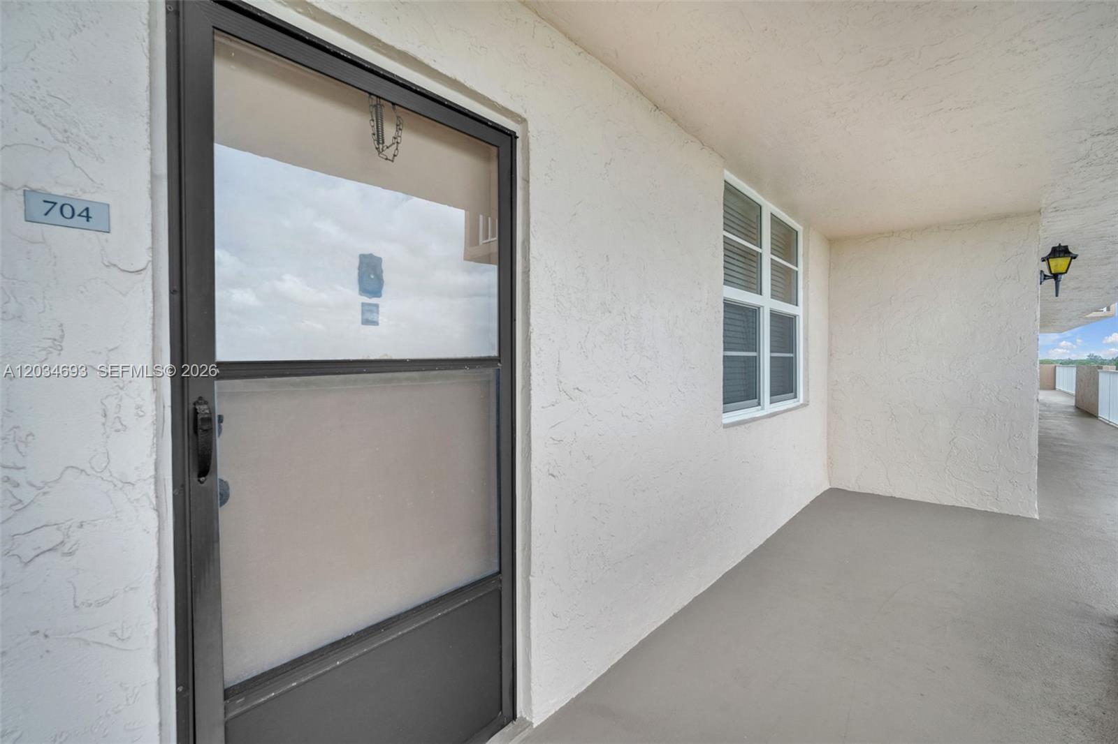 A view of a building exterior showing a unit entrance door, a window, and a walkway — 250 Jacaranda Dr # 704, Plantation FL 33324, PLANTATION, FL