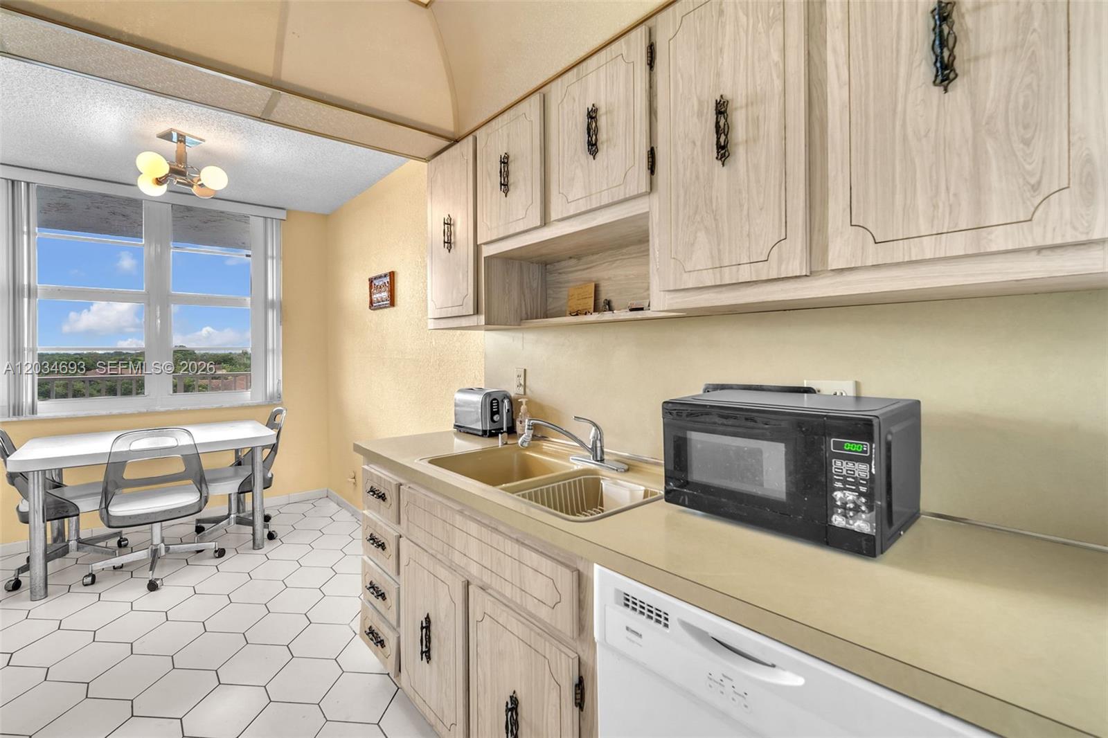 A kitchen features light wood cabinets, a double sink, a microwave, and a dining area — 250 Jacaranda Dr # 704, Plantation FL 33324, PLANTATION, FL