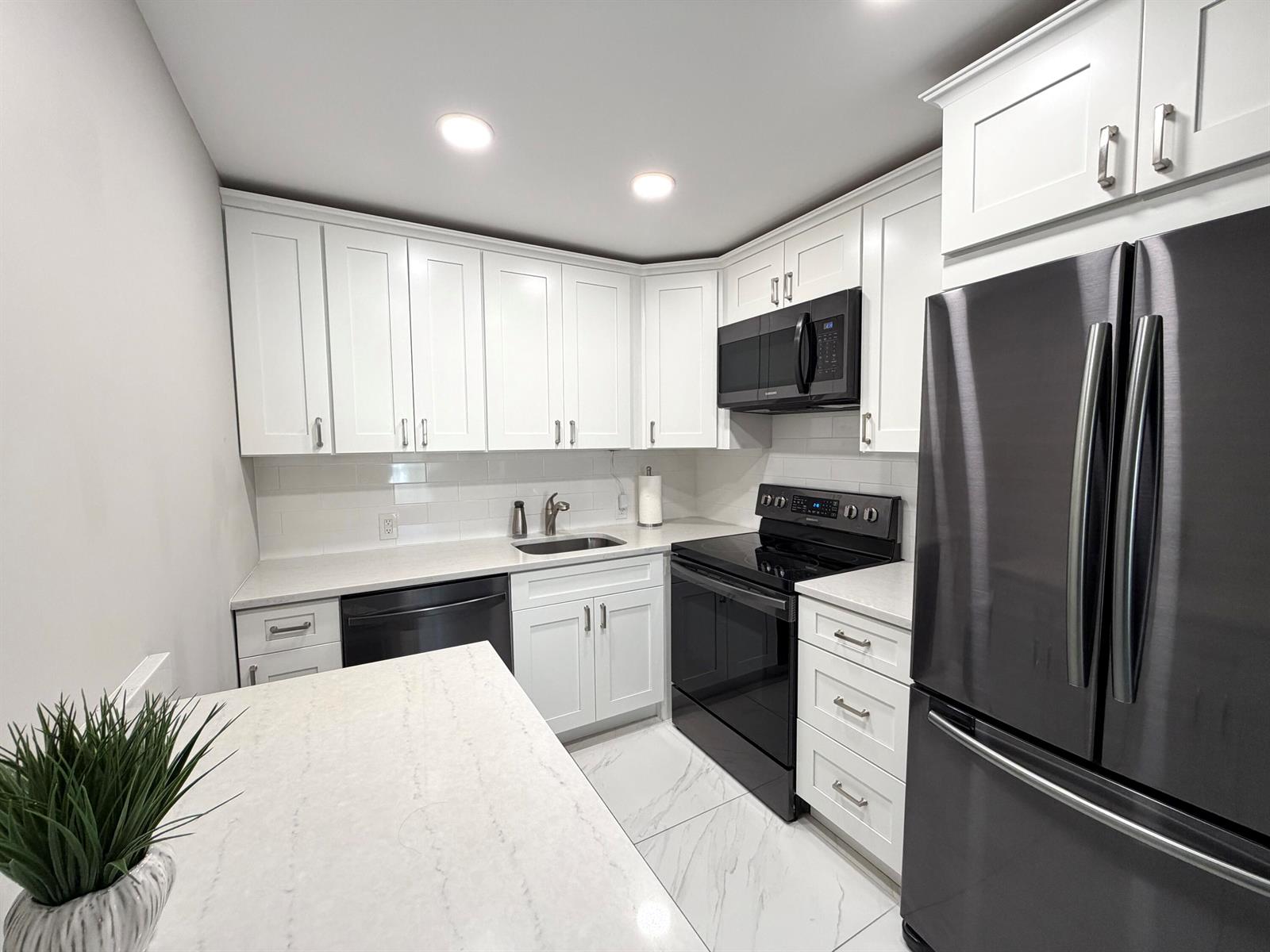 A kitchen features white cabinets, black appliances, quartz countertops, and light-colored tile flooring — 101 Dorset C, Boca Raton FL 33434, BOCA RATON, FL