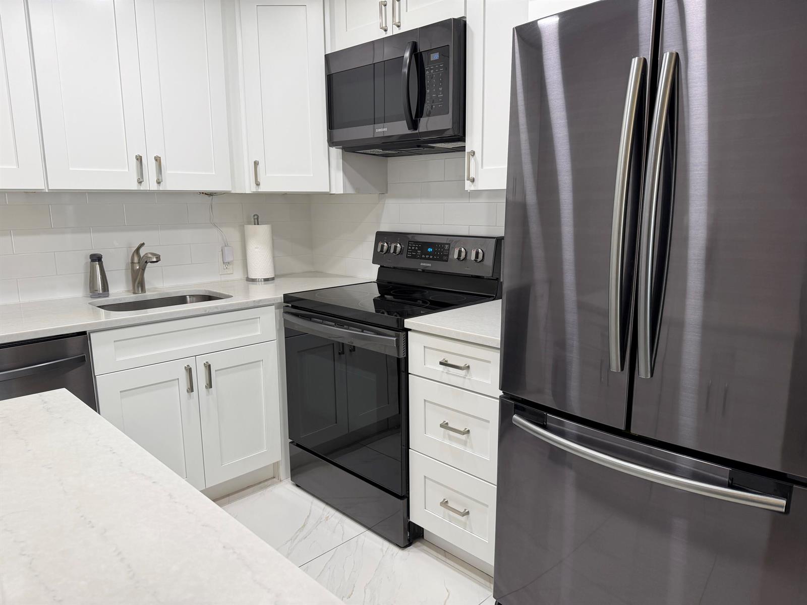 A modern kitchen features white cabinets, stainless steel appliances, and a light-colored countertop — 101 Dorset C, Boca Raton FL 33434, BOCA RATON, FL