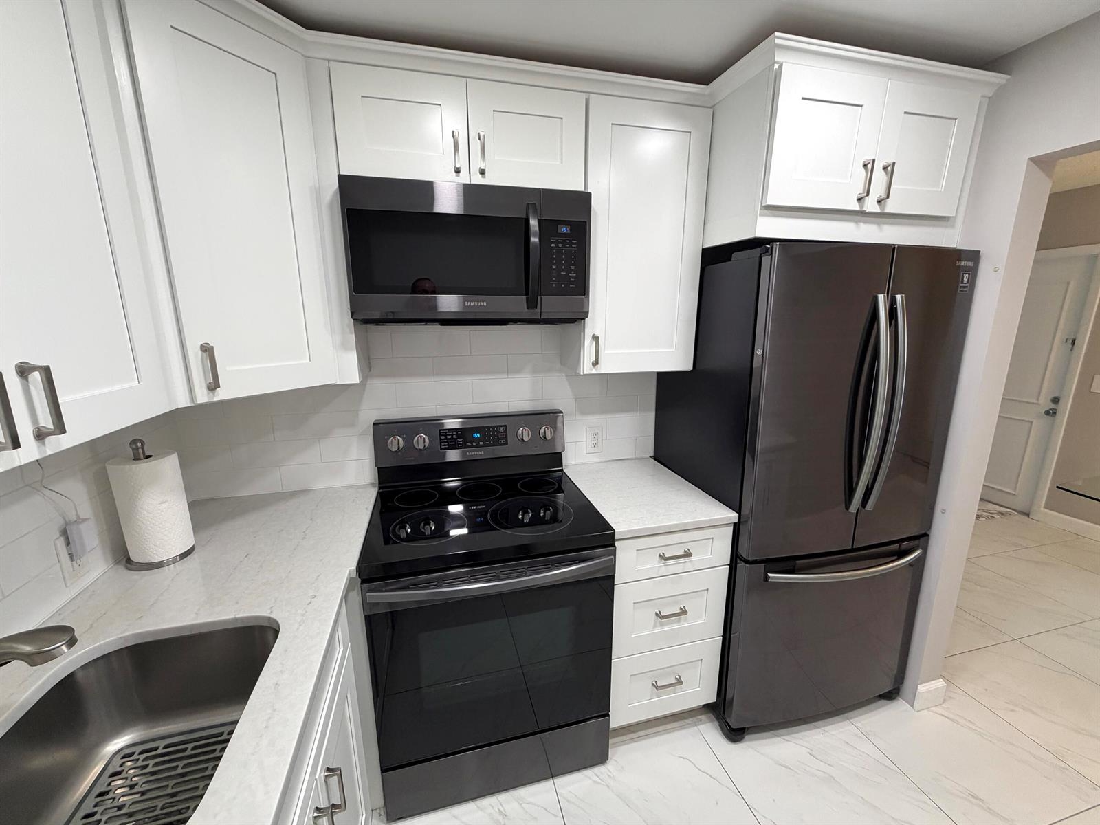 A kitchen features white cabinets, black appliances, a subway tile backsplash, and light countertops — 101 Dorset C, Boca Raton FL 33434, BOCA RATON, FL
