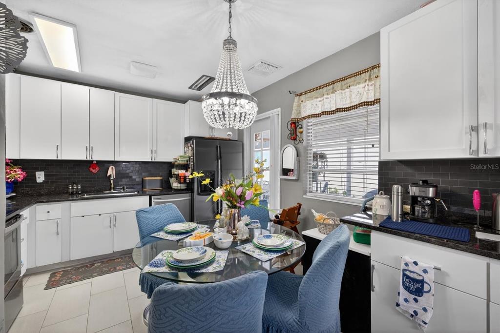 A kitchen with white cabinets, black tile backsplash, and a glass dining table with chairs — 611 N BRADFORD AVENUE, TAMPA, FL
