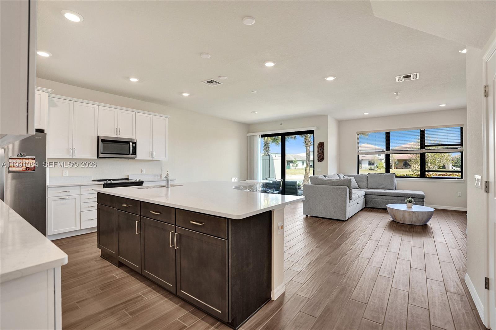 An open-concept kitchen with a dark island and white cabinets overlooks a living area — 4814 Jumping Way, Lake Worth FL 33467, LAKE WORTH, FL