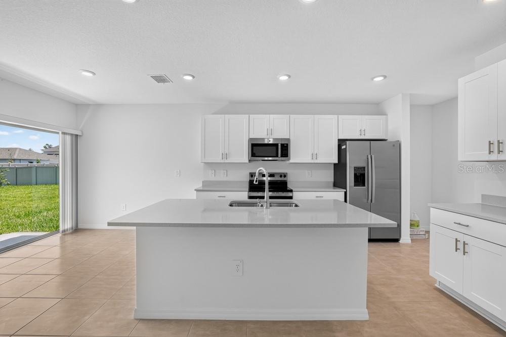 A modern kitchen features white cabinetry, a large central island, and stainless steel appliances — 12411 GUST COURT, HUDSON, FL