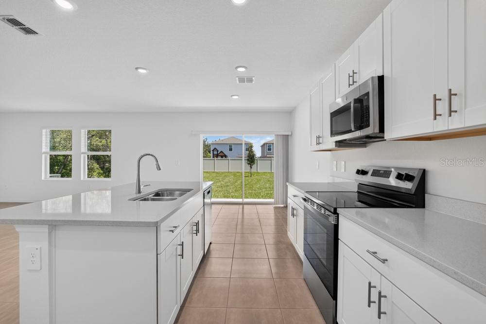 A modern kitchen features white cabinets, a large island with a sink, and tile flooring — 12411 GUST COURT, HUDSON, FL