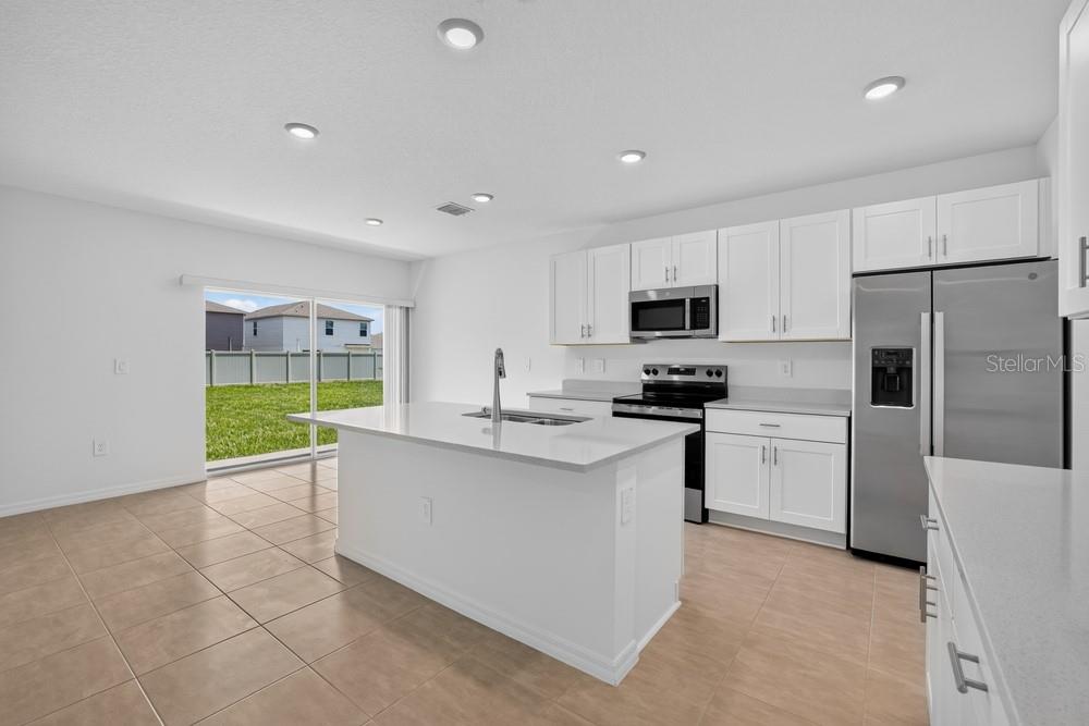 A modern kitchen features white cabinets, stainless steel appliances, a center island, and tile flooring — 12411 GUST COURT, HUDSON, FL