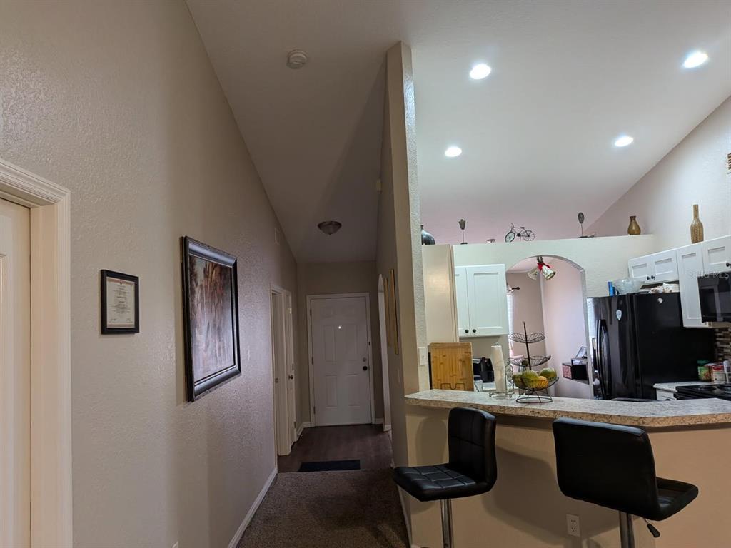 A view from a carpeted hallway looking toward a kitchen with a breakfast bar — 187 CONCH DRIVE, POINCIANA, FL