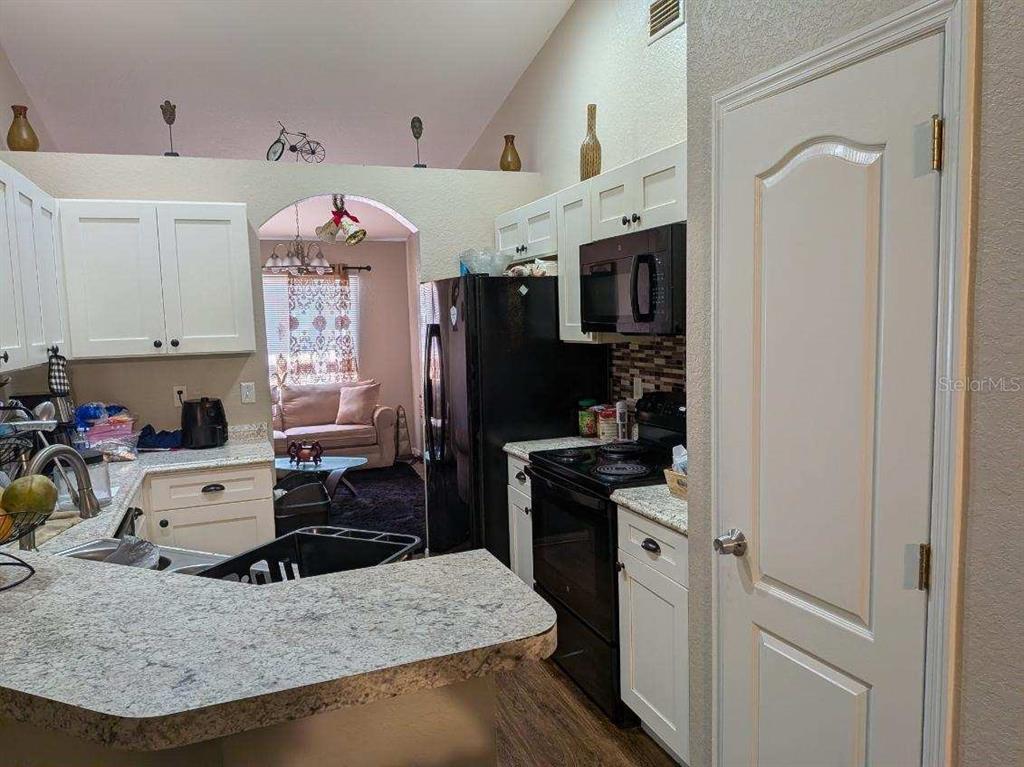 A kitchen with white cabinets, granite countertops, and black appliances overlooks a living area — 187 CONCH DRIVE, POINCIANA, FL