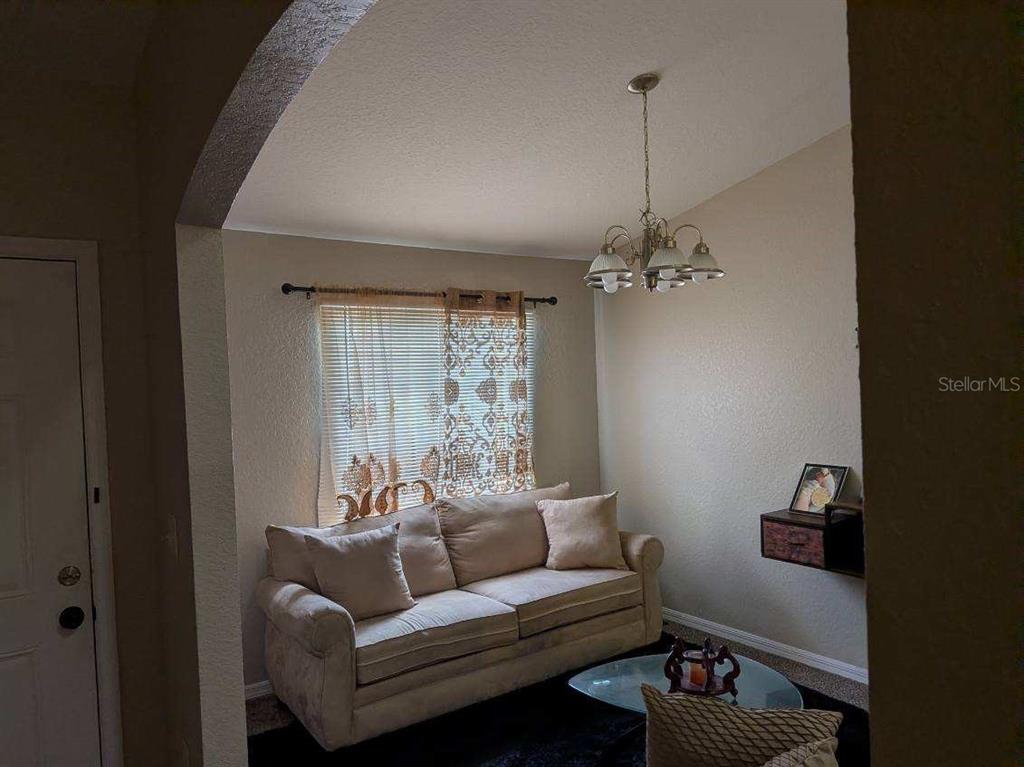 A living room features a beige sofa, a window with patterned curtains, and a chandelier — 187 CONCH DRIVE, POINCIANA, FL