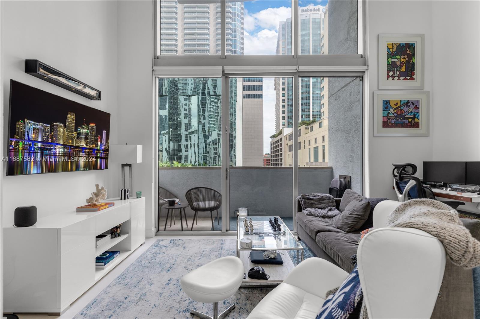 A modern living room features floor-to-ceiling windows, a balcony, and a television mounted above cabinetry — 1060 Brickell Ave # 409, Miami FL 33131, MIAMI, FL