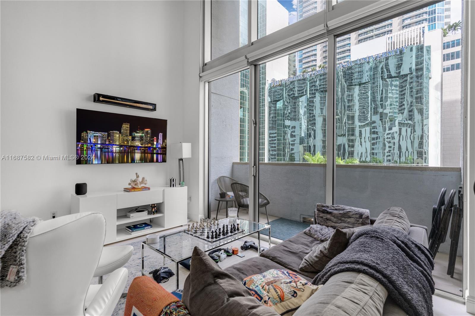 A living room features a television, a glass coffee table, and floor-to-ceiling windows with balcony access — 1060 Brickell Ave # 409, Miami FL 33131, MIAMI, FL