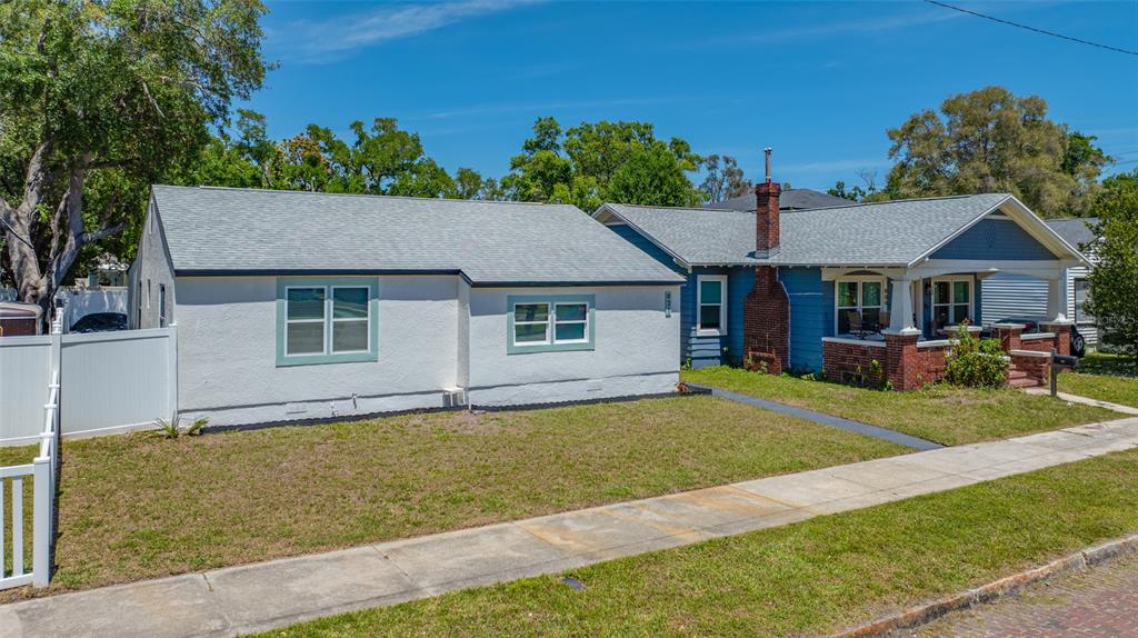 A white stucco house sits next to a blue house with a brick chimney and porch — 821 19TH AVENUE S, ST PETERSBURG, FL