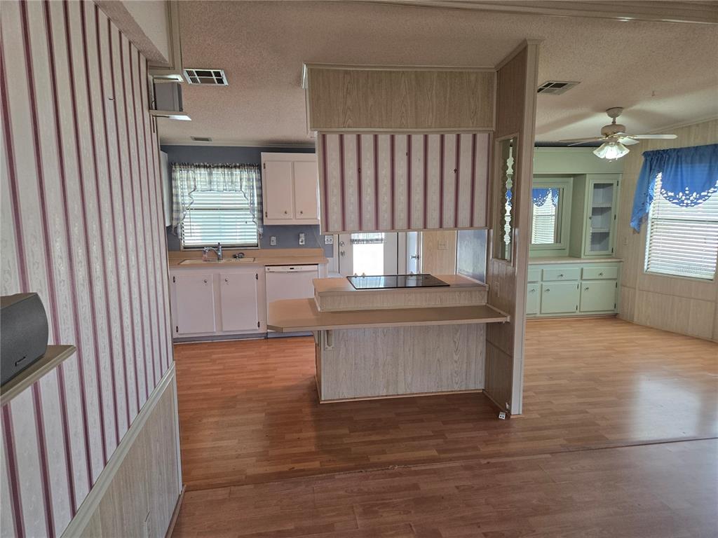A kitchen with wood-look flooring, striped wallpaper, white cabinets, and a central cooktop island — 68 PELICAN DRIVE S, OLDSMAR, FL