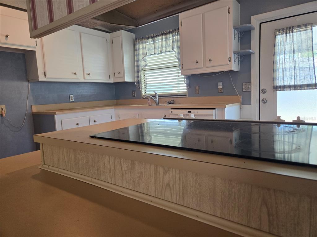 A kitchen features a cooktop island, white cabinets, blue walls, and a light-colored countertop — 68 PELICAN DRIVE S, OLDSMAR, FL