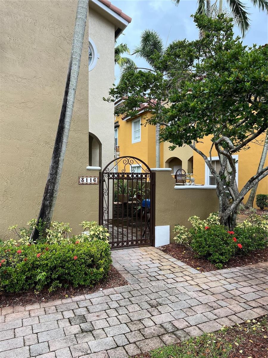 A brown metal gate leads to a courtyard entrance between two stucco buildings — 3116 Merrick Terrace # 3116, Margate FL 33063, MARGATE, FL