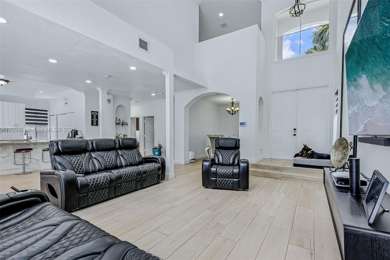 A spacious living room features light wood-look tile floors, high ceilings, and black leather furniture — 13370 SW 32nd St, Miramar FL 33027, MIRAMAR, FL