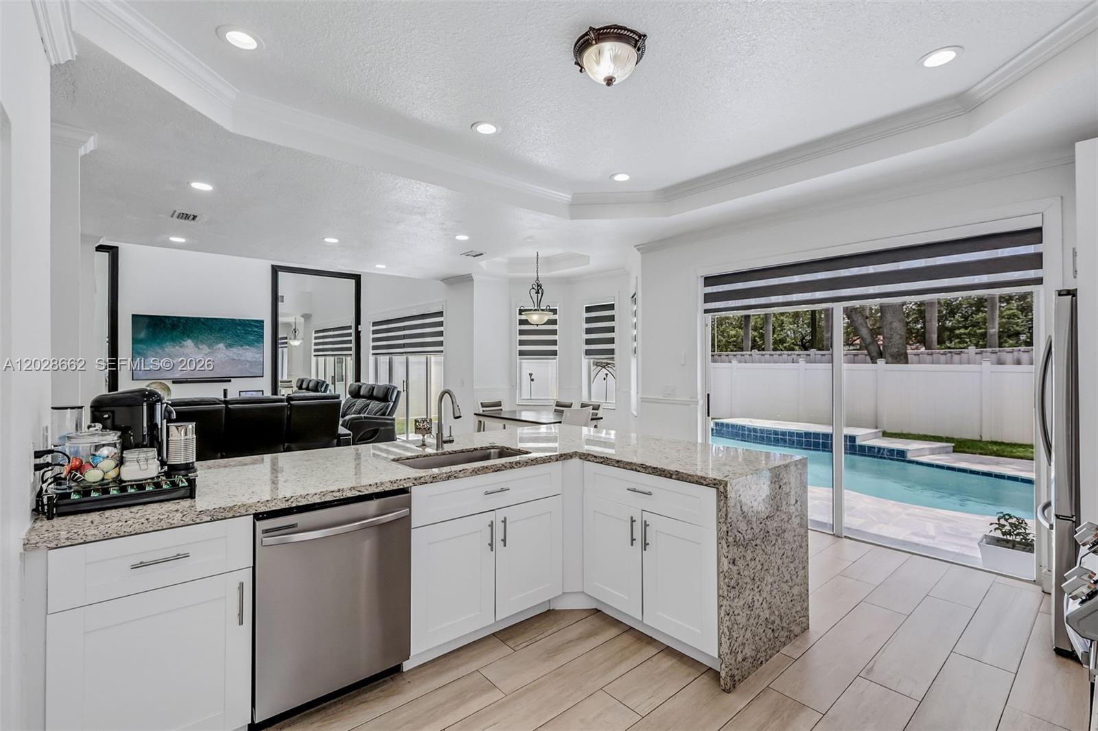 A white kitchen with granite countertops overlooks a backyard swimming pool through sliding glass doors — 13370 SW 32nd St, Miramar FL 33027, MIRAMAR, FL