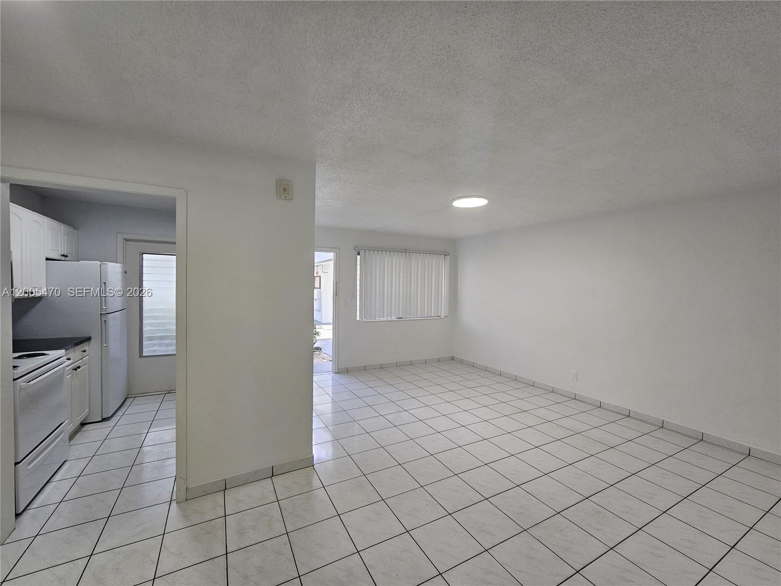 A white-walled room with white tile flooring connects to a kitchen with white appliances — 1719 Wiley St # 2, Hollywood FL 33020, HOLLYWOOD, FL