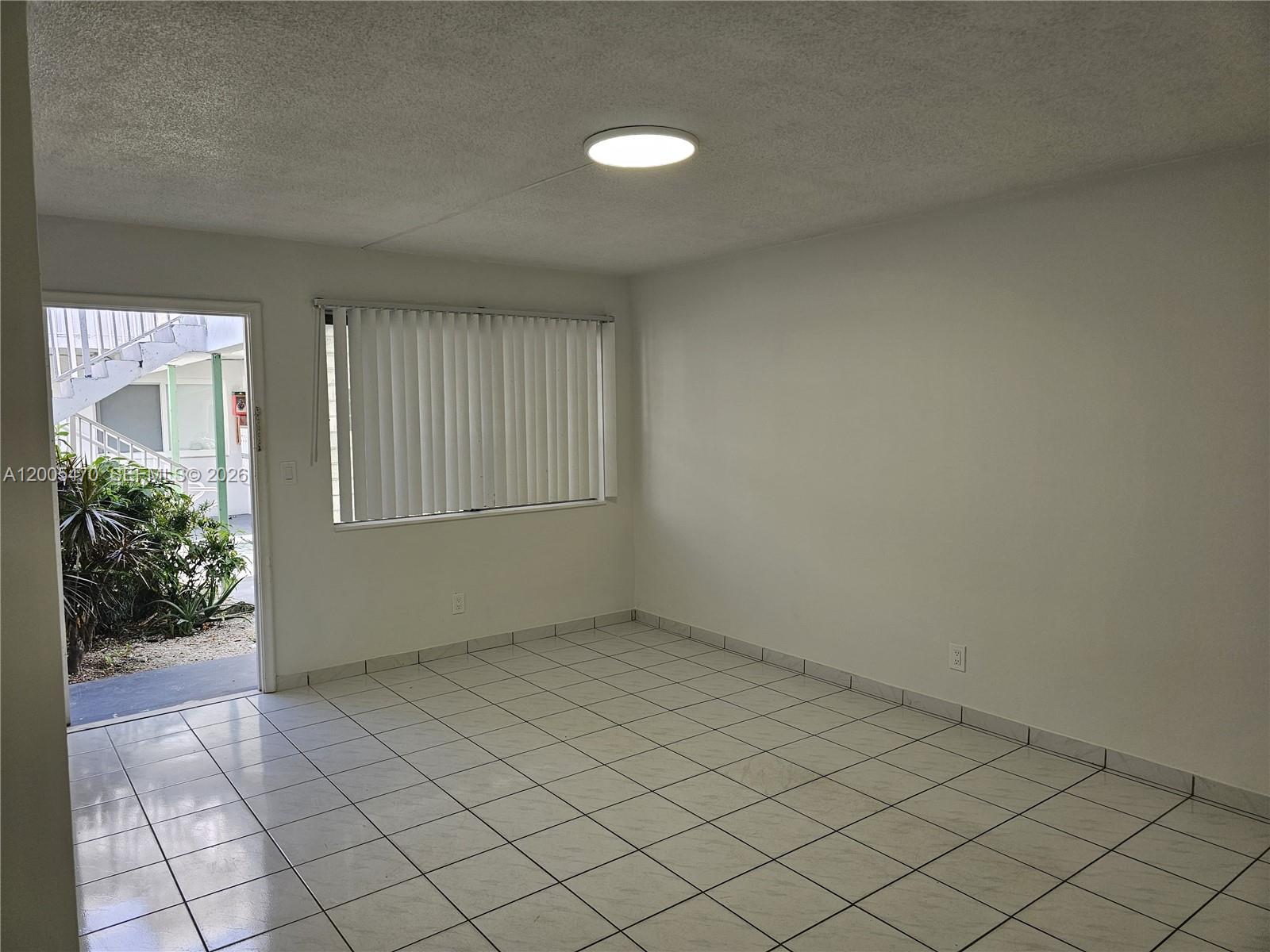 An empty room features white tiled floors, plain walls, a ceiling light, and a glass door — 1719 Wiley St # 2, Hollywood FL 33020, HOLLYWOOD, FL