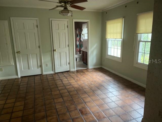 A room with brown tiled flooring, two white doors, and a doorway leading to a bathroom — 1628 NW 6TH AVENUE, GAINESVILLE, FL