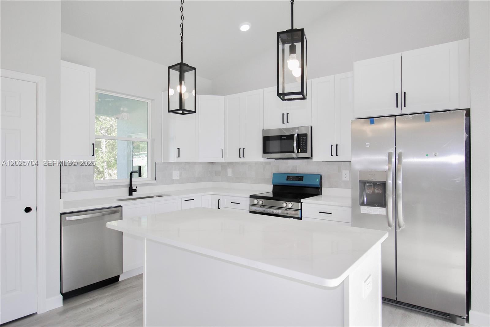 A modern open-concept kitchen and dining area features white cabinetry, stainless appliances, and wood flooring — 4608 CORTEZ BLVD, Sebring FL 33872, SEBRING, FL