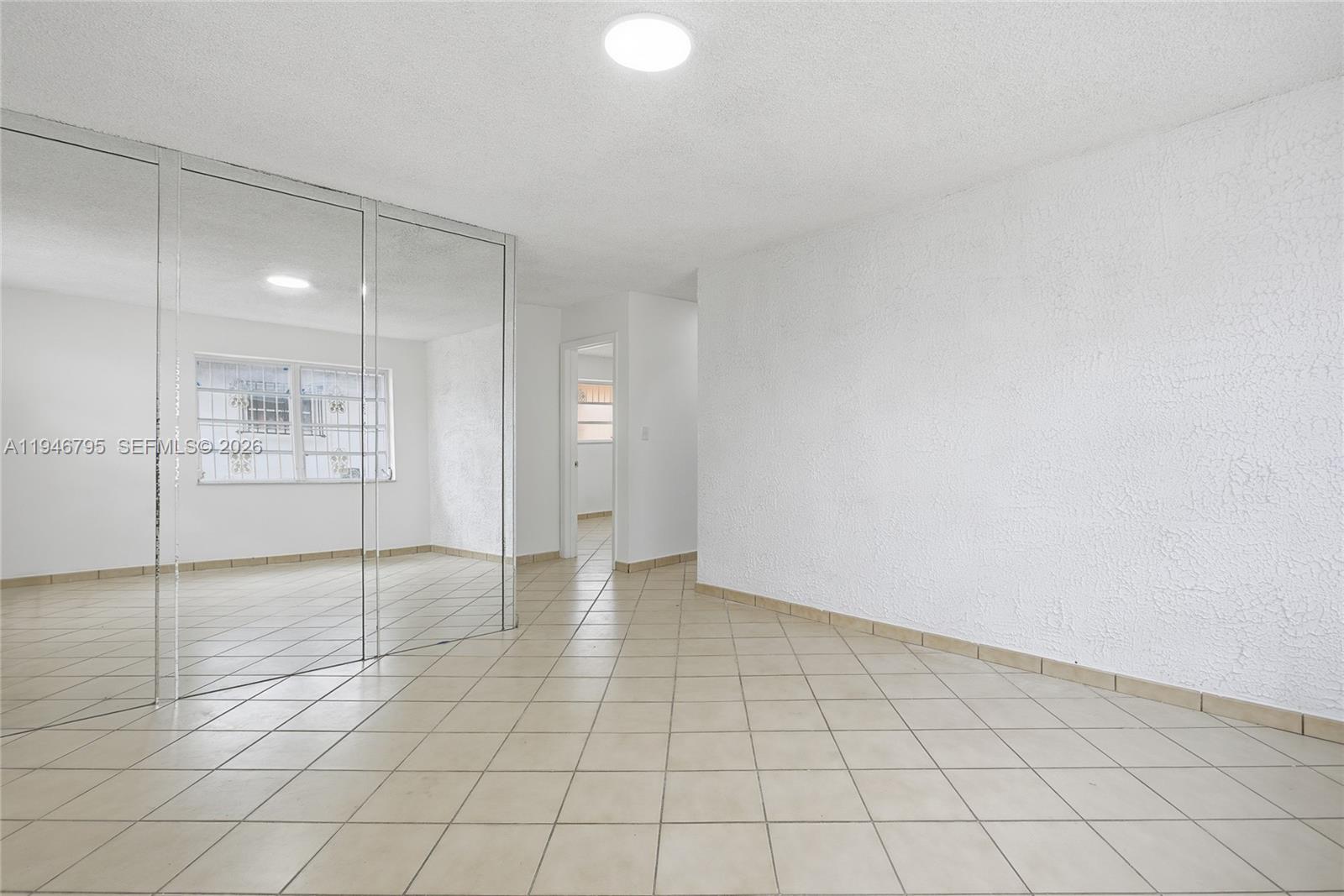 A room with tiled floors, a textured white wall, and mirrored sliding closet doors — 836 W 37th St, Hialeah FL 33012, HIALEAH, FL