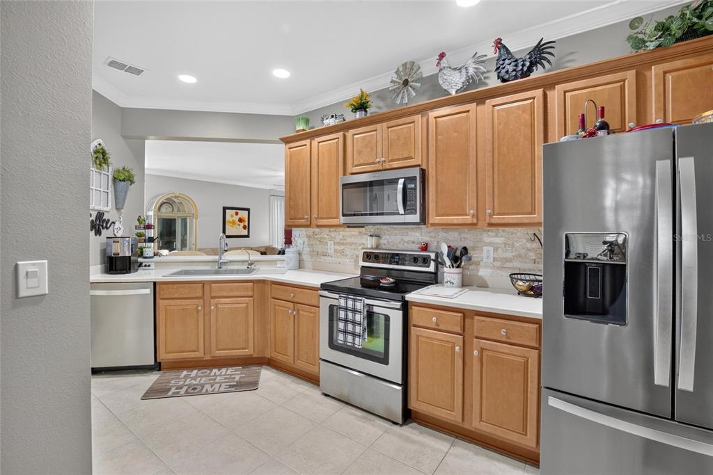 A kitchen features light wood cabinets, stainless steel appliances, and a stone tile backsplash — 342 BLUEWATER FALLS COURT, APOLLO BEACH, FL