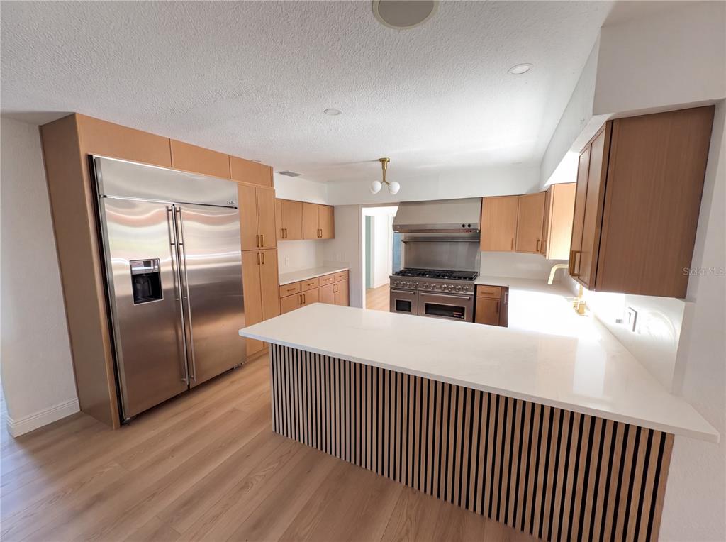 A modern kitchen features light wood cabinets, a slatted island, and stainless steel appliances — 51 OAKLEIGH LANE, MAITLAND, FL