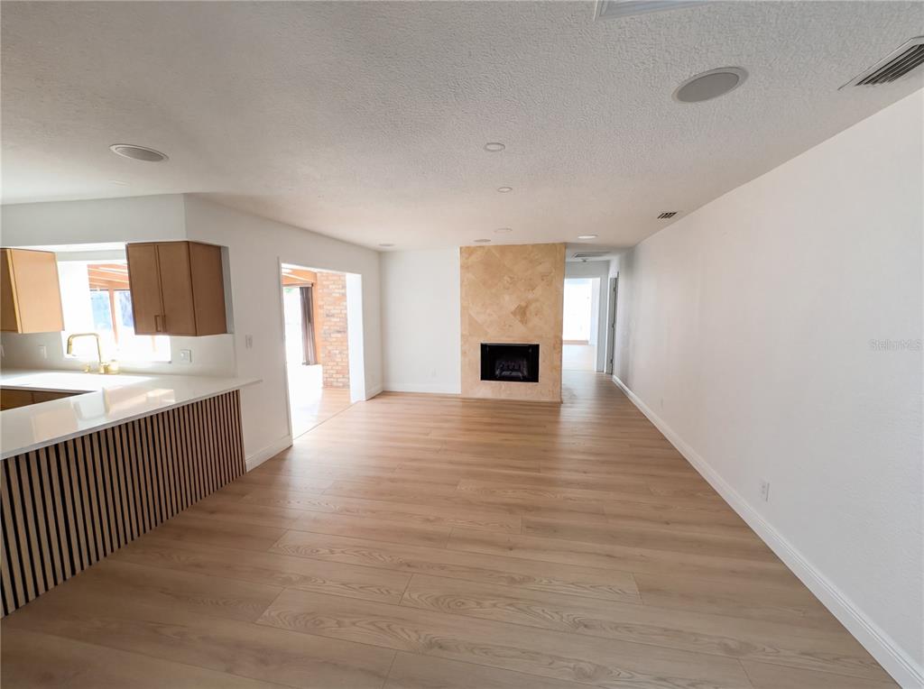 A living room with light wood flooring, a stone fireplace, and an adjacent kitchen area — 51 OAKLEIGH LANE, MAITLAND, FL