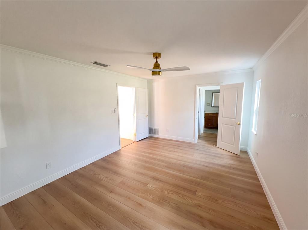 A bedroom with light wood-look flooring, white walls, a ceiling fan, and two open doorways — 51 OAKLEIGH LANE, MAITLAND, FL
