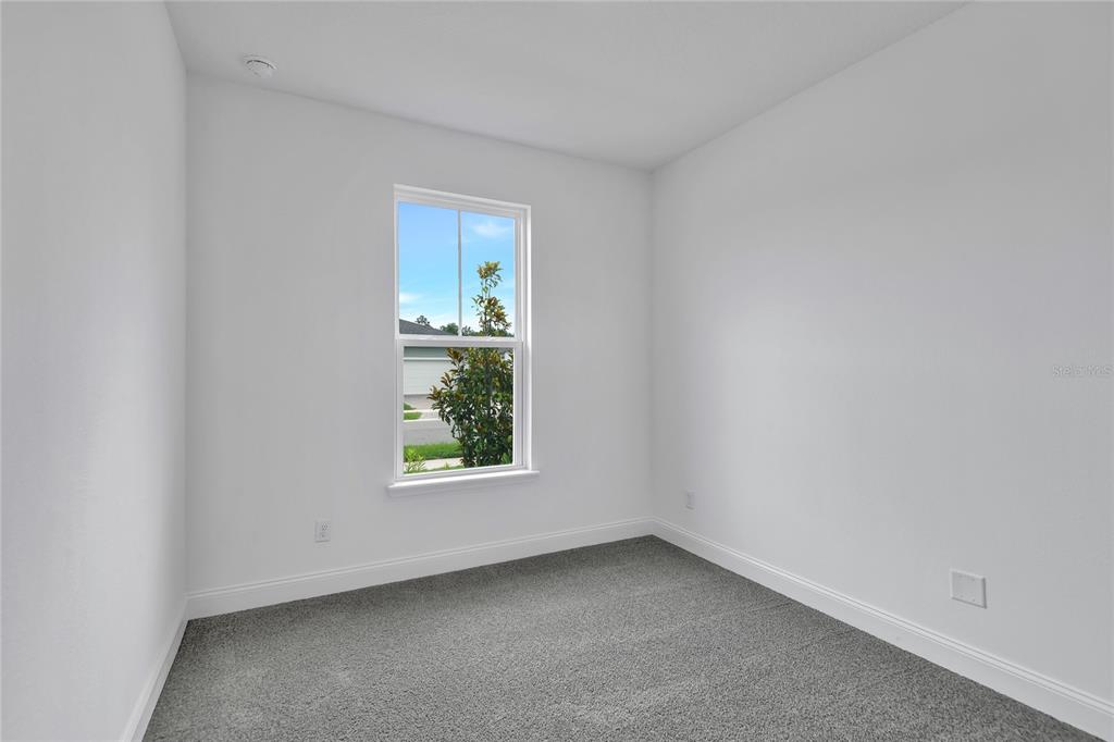 A small, empty bedroom features white walls, gray carpeting, and a single window — 206 ENCLAVE AVENUE, PALM COAST, FL