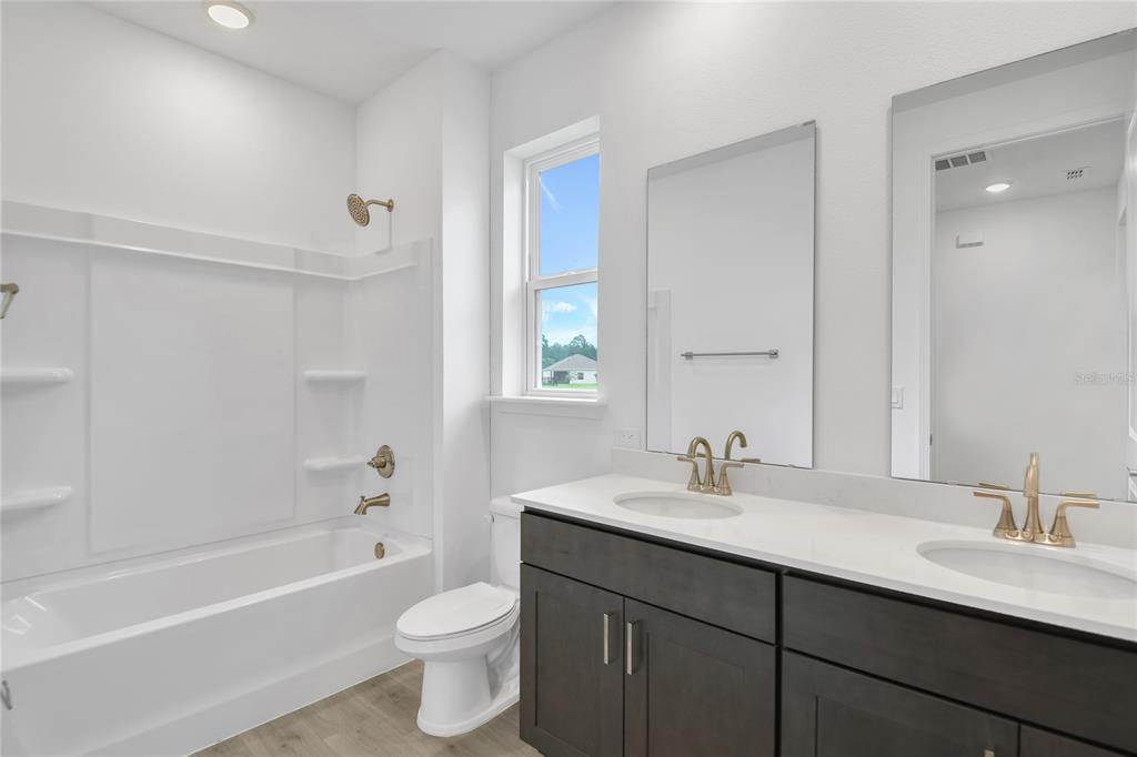 A modern bathroom features a double vanity, a white tub-shower combo, and a toilet — 206 ENCLAVE AVENUE, PALM COAST, FL
