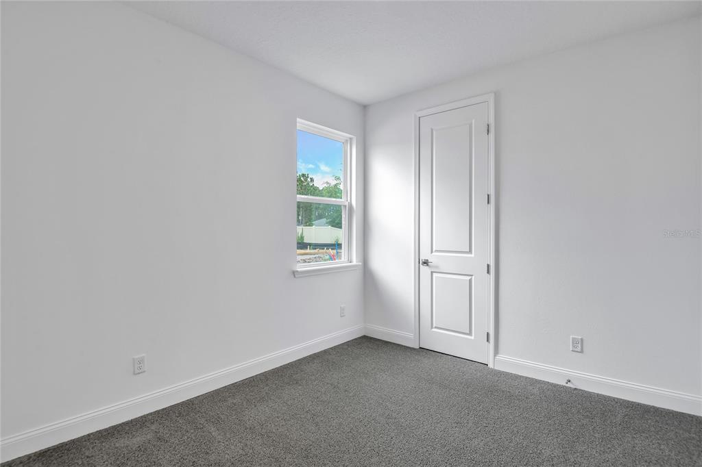 A bedroom with white walls, gray carpet, a single window, and a white door — 206 ENCLAVE AVENUE, PALM COAST, FL