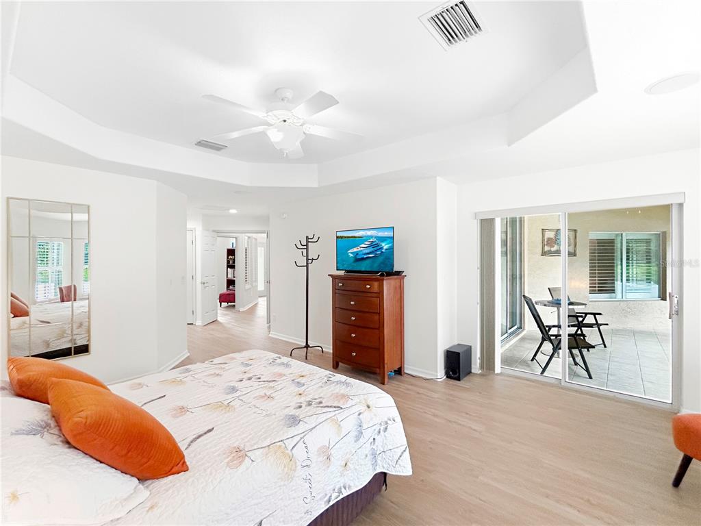 A bedroom features a tray ceiling, light wood flooring, and sliding glass doors to a patio — 2716 SW 20TH AVENUE, OCALA, FL
