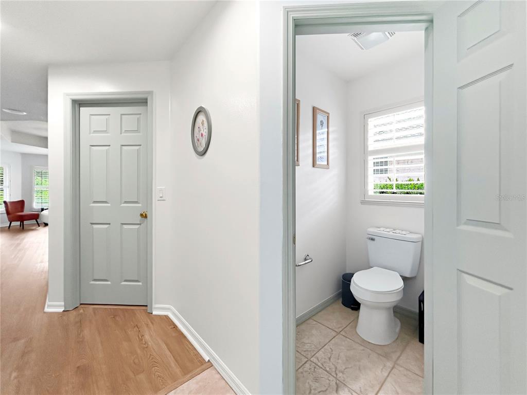A hallway with wood-look flooring leads to a closed door and a small bathroom — 2716 SW 20TH AVENUE, OCALA, FL