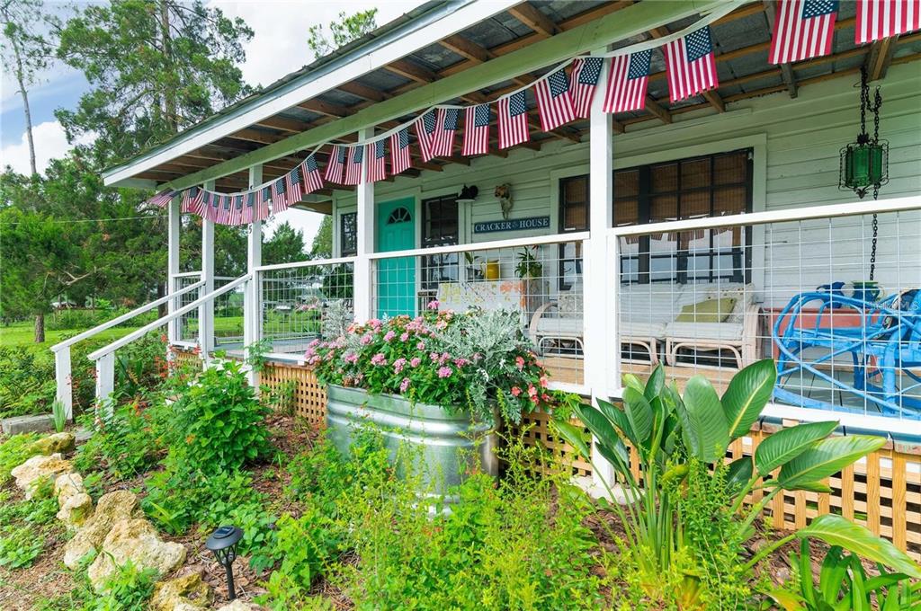 A porch with a metal roof, American flag bunting, and a galvanized planter with flowers — 39425 WILDS ROAD, DADE CITY, FL