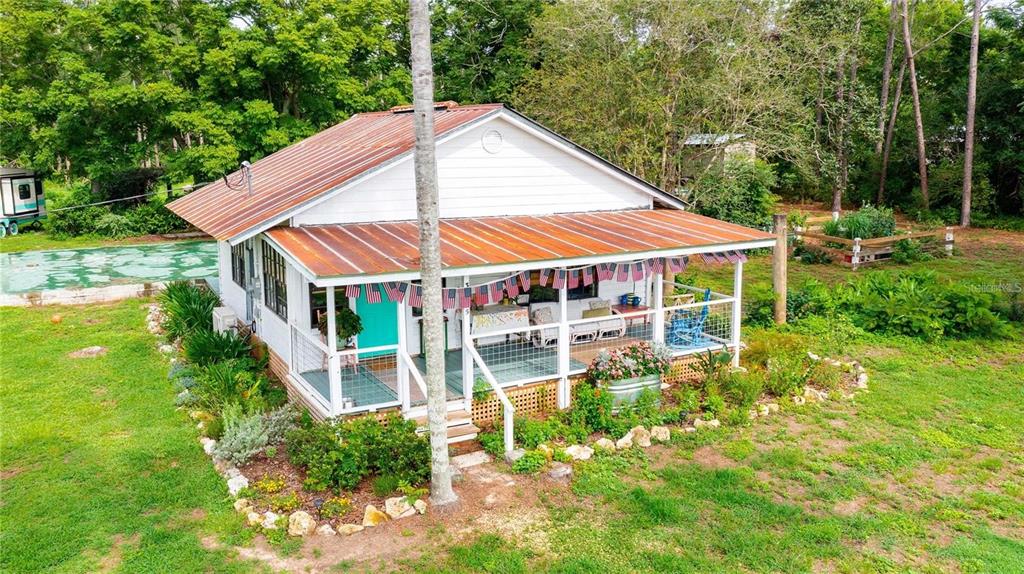An elevated exterior view of a white cottage with a rusted metal roof and porch — 39425 WILDS ROAD, DADE CITY, FL