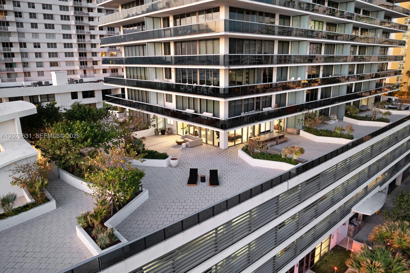 An elevated view shows a large paved terrace with lounge chairs and planters beside a building — 5875 Collins Ave # 501, Miami Beach FL 33140, MIAMI BEACH, FL