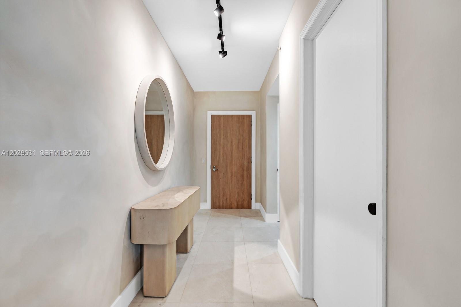 A hallway features a wooden console table, a round mirror, and a wooden door — 5875 Collins Ave # 501, Miami Beach FL 33140, MIAMI BEACH, FL
