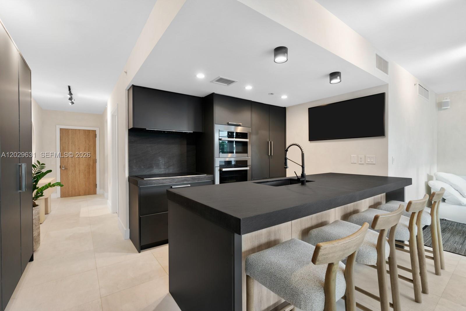 A modern kitchen features dark cabinetry, a large island with bar seating, and light flooring — 5875 Collins Ave # 501, Miami Beach FL 33140, MIAMI BEACH, FL