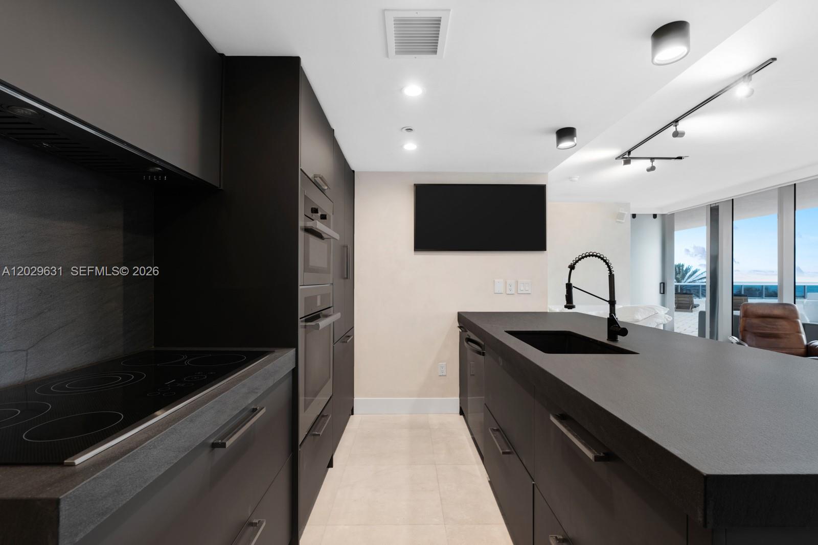 A modern kitchen features dark cabinetry, a central island with a sink, and stainless appliances — 5875 Collins Ave # 501, Miami Beach FL 33140, MIAMI BEACH, FL