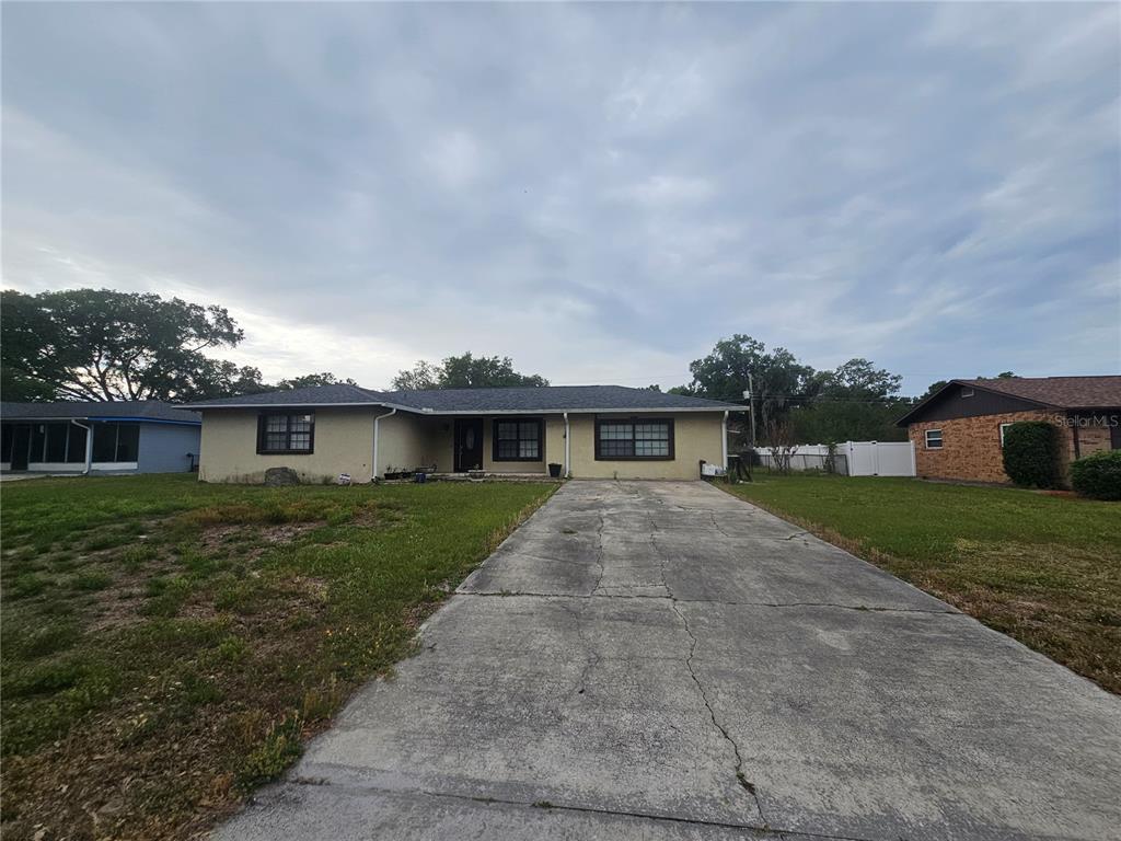 A single-story house with a concrete driveway, a tan stucco exterior, and a dark roof — 204 JENNY WAY, LAKELAND, FL