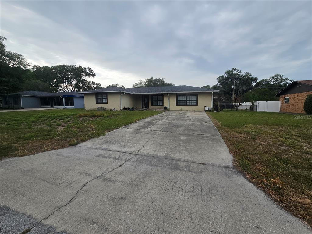 A single-story house with a concrete driveway and a tan exterior sits under a cloudy sky — 204 JENNY WAY, LAKELAND, FL