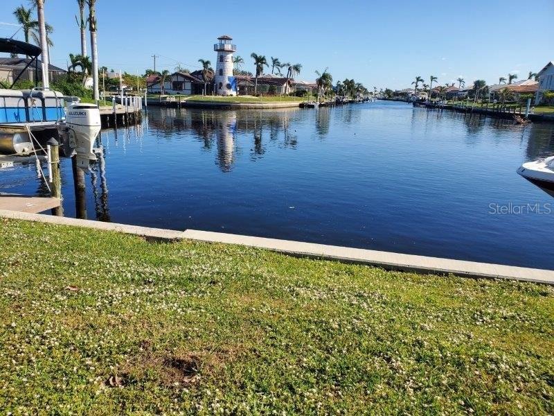 A canal view features a lighthouse, palm trees, and a boat docked in the foreground — 418 MEDICI COURT, PUNTA GORDA, FL