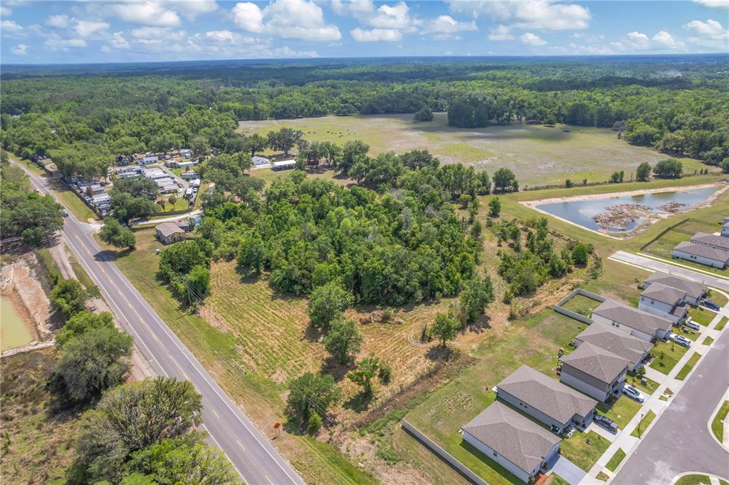 An aerial view shows a vacant wooded lot situated between a road and residential homes — CORNER OF PAUL S BUCHMAN HWY & FORREST PLUM CT, ZEPHYRHILLS, FL